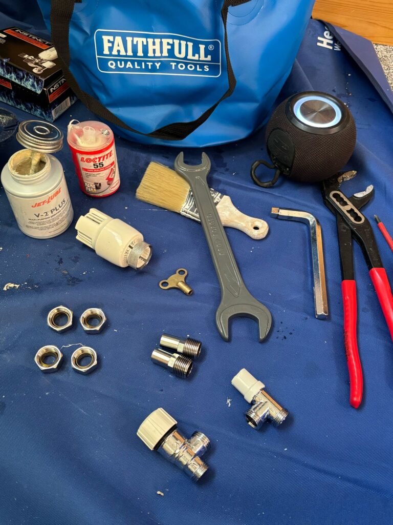 Radiator valves, fittings and plumbing tools laid out on a protective mat